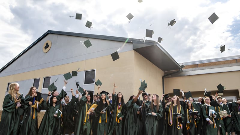 Eine Gruppe von Absolventinnen und Absolventen der Centenary Heights State High School feiert vor dem Schulgebäude ihren Abschluss.