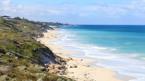 Eine Küstenlandschaft mit Sandstrand, Felsen und türkisfarbenem Meer unter blauem Himmel.
