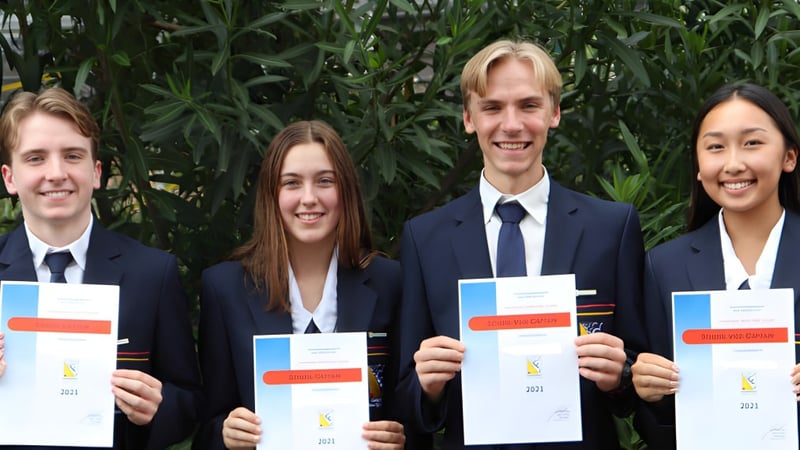 Vier Schülerinnen und Schüler der Centenary State High School halten ihre Diplome vor grünem Hintergrund.
