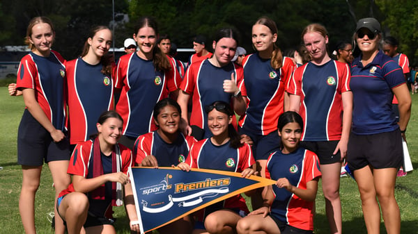 Eine Gruppe Schüler der Centenary State High School posiert gemeinsam auf einem Sportfeld mit einem Banner im Vordergrund.