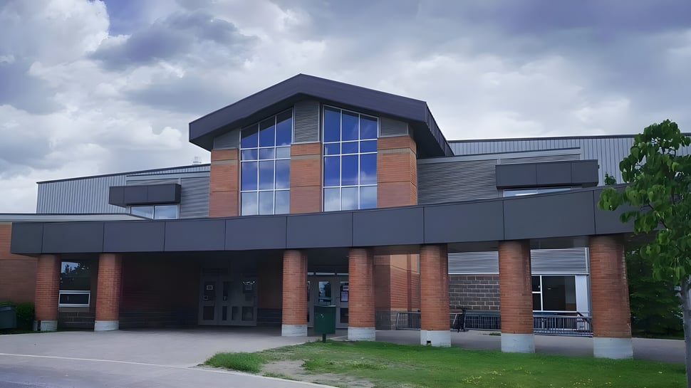 Das moderne mehrstöckige Gebäude des Centennial Collegiate mit einer Fassade aus Backstein und Glas steht umgeben von Rasenflächen und Bäumen.
