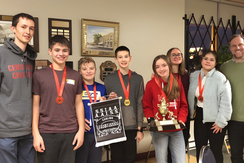 Eine Gruppe Schülerinnen und Schüler der Centennial Regional High School hält im Schulgebäude verschiedene Auszeichnungen und Pokale.