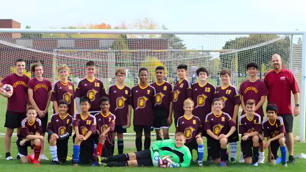 Eine Gruppe Schülerinnen und Schüler der Centennial Regional High School posiert gemeinsam auf einem Fußballfeld mit der Stadtsilhouette im Hintergrund.