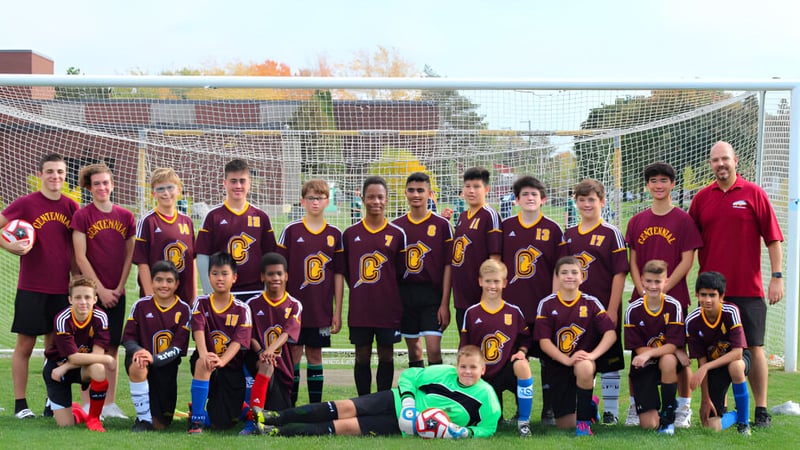 Eine Gruppe Schülerinnen und Schüler der Centennial Regional High School posiert gemeinsam auf einem Fußballfeld mit der Stadtsilhouette im Hintergrund.
