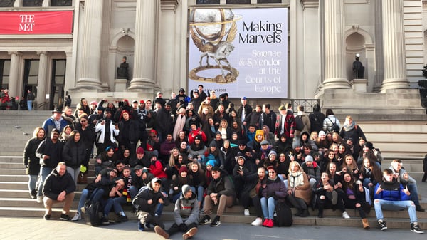 Eine große Gruppe von Schülerinnen und Schülern versammelt sich vor dem Gebäude der Centennial Regional High School mit dem Banner 'Making Miracles'.