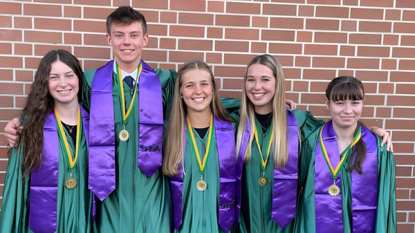Absolventinnen und Absolventen der Centennial Secondary School in Ontario stehen in traditionellen Abschlussroben vor einer Backsteinmauer.