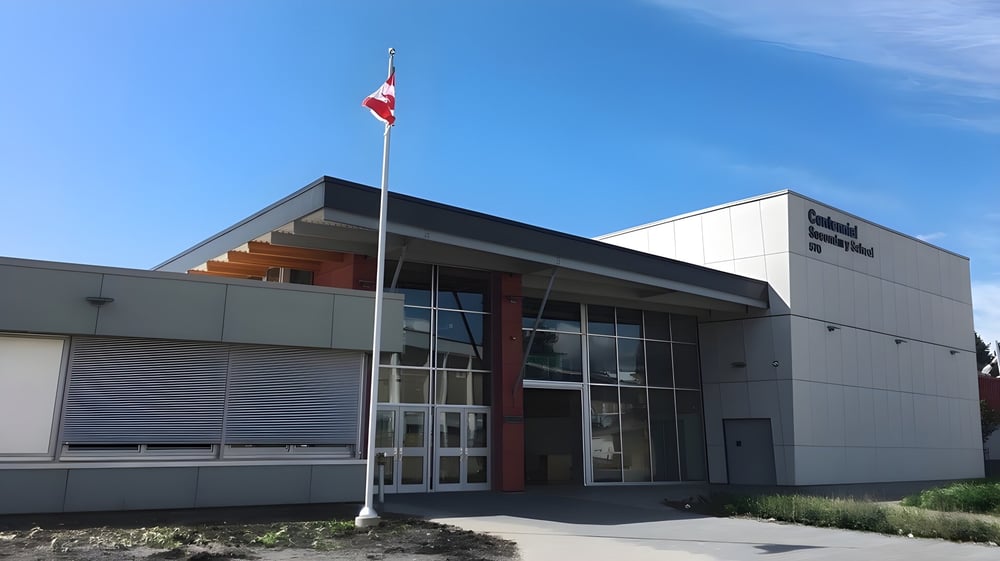 Das moderne Gebäude der Centennial Secondary School in British Columbia mit einer kanadischen Flagge vor klarem blauem Himmel.