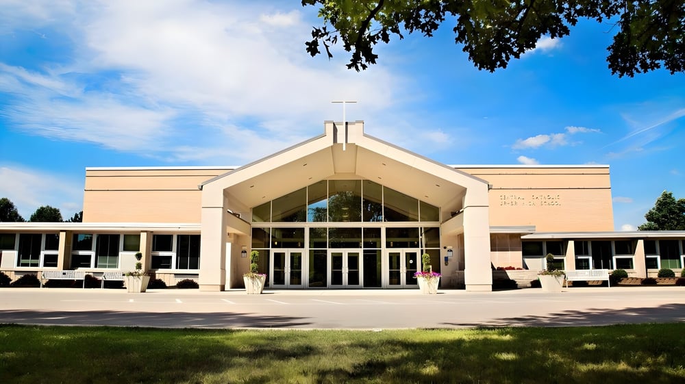Das moderne Hauptgebäude der Central Catholic Jr.-Sr. High School mit großen Fenstern und umliegender Grünfläche unter blauem Himmel.