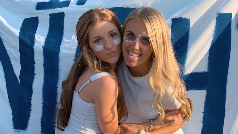 Zwei Schülerinnen der Central Catholic Jr.-Sr. High School umarmen sich vor einem blau-weißen abstrakten Hintergrund.