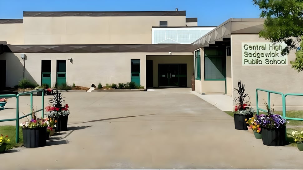 Das moderne Schulgebäude der Central High Sedgewick Public School mit gepflastertem Eingang und Blumen ist von Bäumen umgeben.