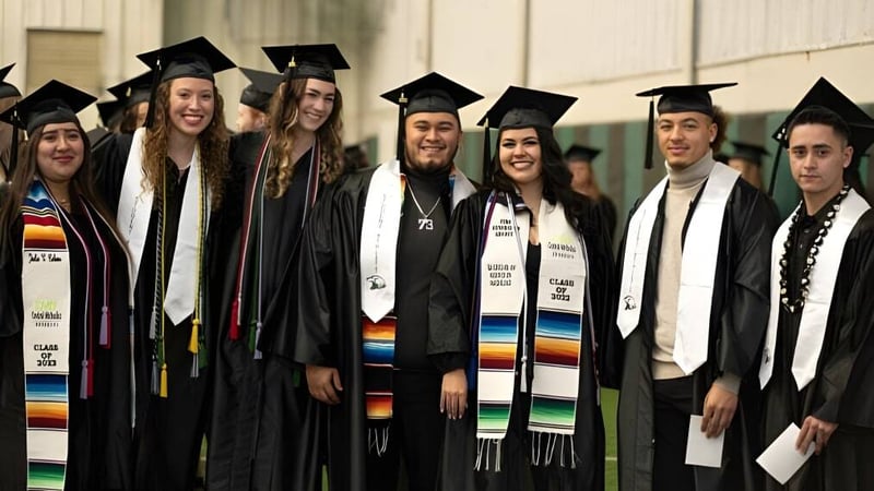 Eine Gruppe von Absolventinnen und Absolventen in Talaren steht gemeinsam vor einem einfachen Hintergrund auf dem Campus der Central Methodist University.
