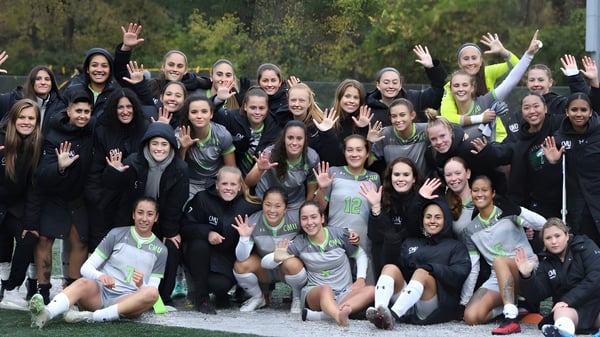 Eine Gruppe junger Frauen in Sportkleidung winkt im Freien vor einem bewaldeten Hintergrund auf dem Campus der Central Methodist University.