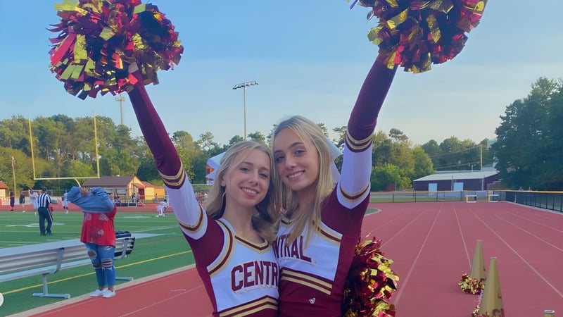 Zwei Cheerleader der Central Regional High School stehen mit Pompons auf dem Sportfeld vor dem Stadion.