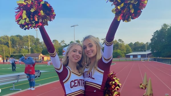 Zwei Cheerleader der Central Regional High School stehen mit Pompons auf dem Sportfeld vor dem Stadion.