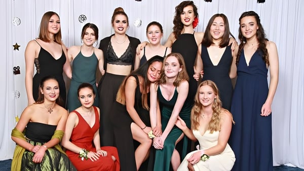 Eine Gruppe junger Schülerinnen des Central Southland College posiert in verschiedenen formellen Kleidern vor einer weiß dekorierten Wand.