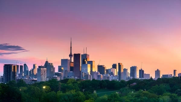 Ein lebendiges Stadtbild mit Hochhäusern vor dem Sonnenuntergang, umgeben von grüner Vegetation, dargestellt ohne direkten Bezug zur Central Toronto Academy.
