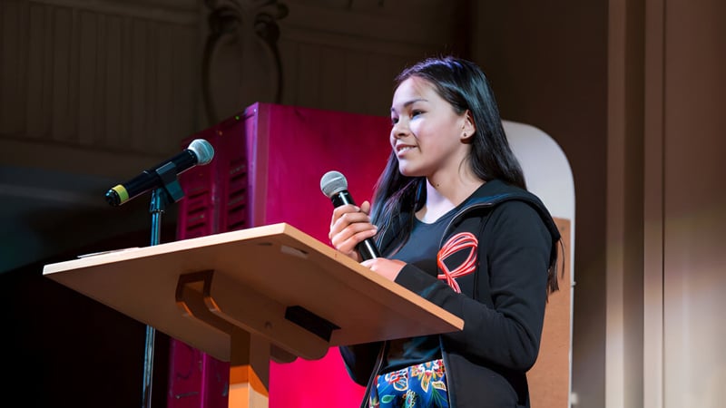 Eine junge Frau spricht am Rednerpult vor rotem Hintergrund auf dem Campus der Central Toronto Academy.