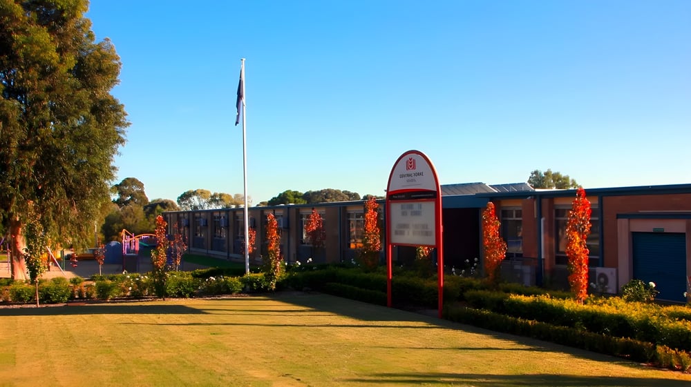 Das Backsteingebäude der Central Yorke School steht vor grüner Umgebung mit einem hohen Fahnenmast und einem gepflasterten Weg.