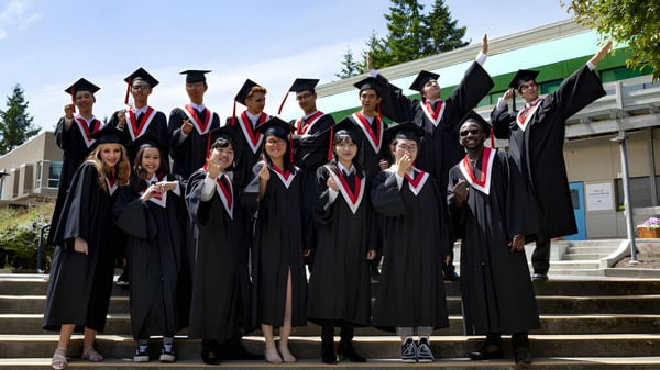 Absolventen der Centre Dufferin District High School stehen in schwarzen Talaren mit roten Schärpen auf der Treppe des Schulgebäudes.