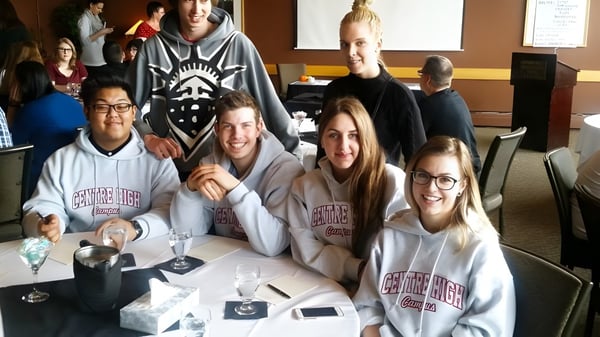 Eine Gruppe Schülerinnen und Schüler sitzt am Tisch im Klassenraum des Centre High Campus mit Getränken und elektronischen Geräten.