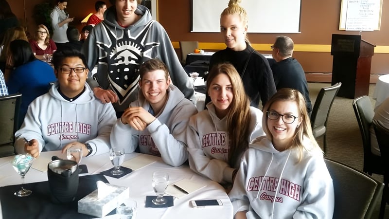 Eine Gruppe Schülerinnen und Schüler sitzt am Tisch im Klassenraum des Centre High Campus mit Getränken und elektronischen Geräten.