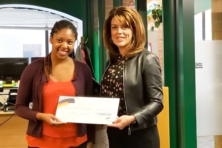 Zwei Schülerinnen halten auf dem Centre High Campus gemeinsam ein Zertifikat vor einer grünen Wand mit Ausstellungsgegenständen.