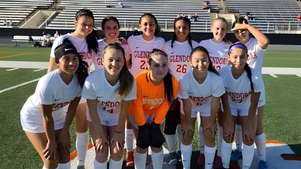 Eine Gruppe von jungen Fußballspielerinnen posiert gemeinsam auf dem Sportplatz der Chaffey High School mit Stadion im Hintergrund.