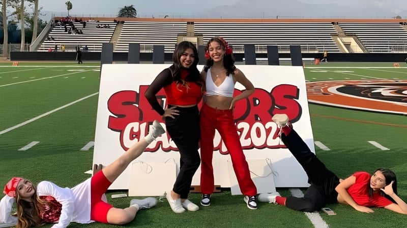 Zwei Schülerinnen der Chaffey High School posieren vor einem Sports Club 2022 Schild auf dem Sportplatz mit Stadion im Hintergrund.