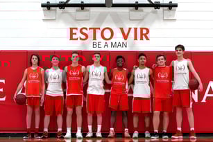 Die Basketballmannschaft der Chaminade College Preparatory School posiert gemeinsam vor einem roten Hintergrund mit dem Schriftzug ESTO VIR BE A MAN.