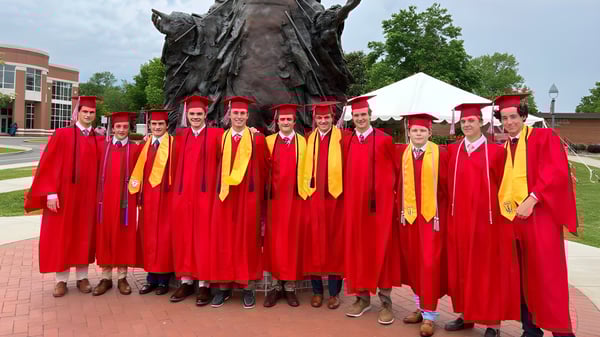 Eine Gruppe von Absolventen in roten und gelben Roben steht vor einer großen bronzenen Statue auf dem Campus der Chaminade College Preparatory School.