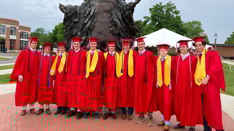 Eine Gruppe von Absolventen in roten und gelben Roben steht vor einer großen bronzenen Statue auf dem Campus der Chaminade College Preparatory School.