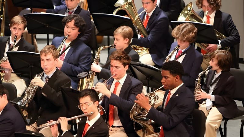Das Orchester der Chaminade College Preparatory School spielt in formeller Kleidung auf einer Bühne vor dunklem Hintergrund.