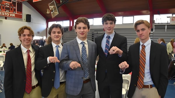 Eine Gruppe von Schülern der Chaminade College Preparatory School steht in formeller Kleidung in einem schulischen Umfeld mit Basketballkorb im Hintergrund.