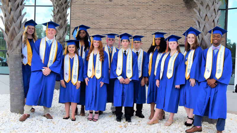 Absolventinnen und Absolventen des Chancellor State College feiern vor einem Backsteingebäude ihren Abschluss.