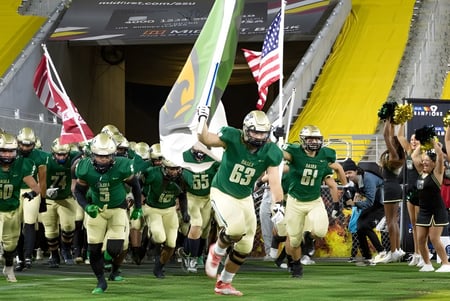 Eine Gruppe Footballspieler in grünen Uniformen läuft auf das Spielfeld beim Chandler Unified School District.