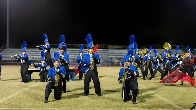 Eine Gruppe von Schülern des Chandler Unified School District steht in blauen und schwarzen Uniformen auf einem Feld vor einer stadionähnlichen Struktur.