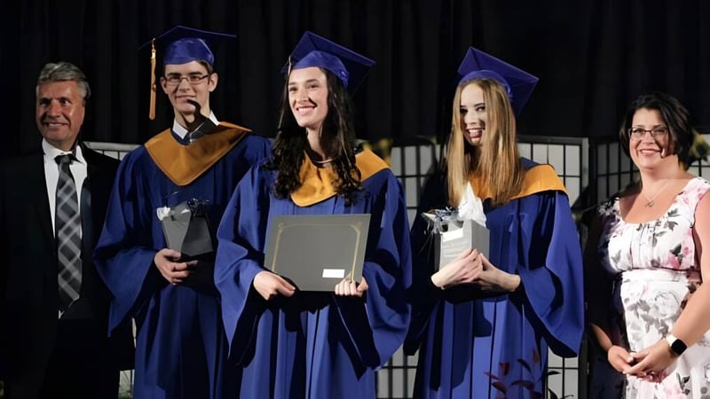 Absolventen der Char-Lan District High School stehen in blauen Talaren auf der Bühne mit Lehrkräften im Hintergrund.