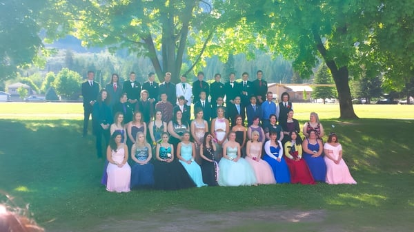 Eine große Gruppe von Schülerinnen und Schülern der Charles Bloom Secondary School versammelt sich im Freien auf einer Wiese mit Bäumen im Hintergrund.