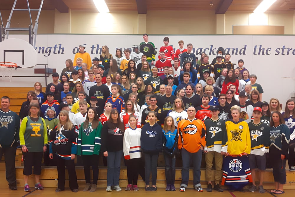 Eine Gruppe Schülerinnen und Schüler in der Turnhalle der Charles Bloom Secondary School vor einer motivationalen Wandbotschaft.