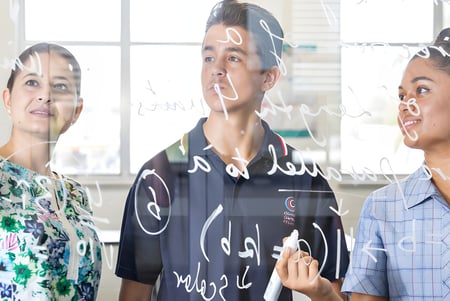 Drei Personen stehen in einem Raum mit großer Fensterfront auf dem Campus des Charles Campbell College.