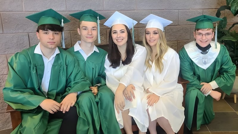 Eine Gruppe von fünf Absolventen in grünen Talaren posiert vor einer Backsteinwand an der Charles Finney School.