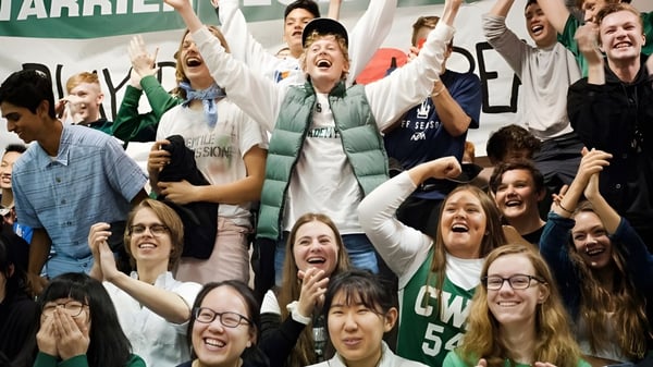 Eine große Gruppe von Schülern der Charles Wright Academy feiert gemeinsam mit erhobenen Armen in einem Innenraum.