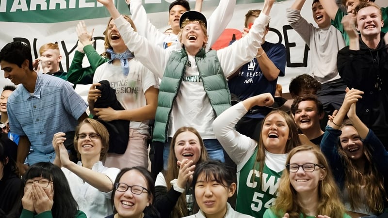 Eine große Gruppe von Schülern der Charles Wright Academy feiert gemeinsam mit erhobenen Armen in einem Innenraum.