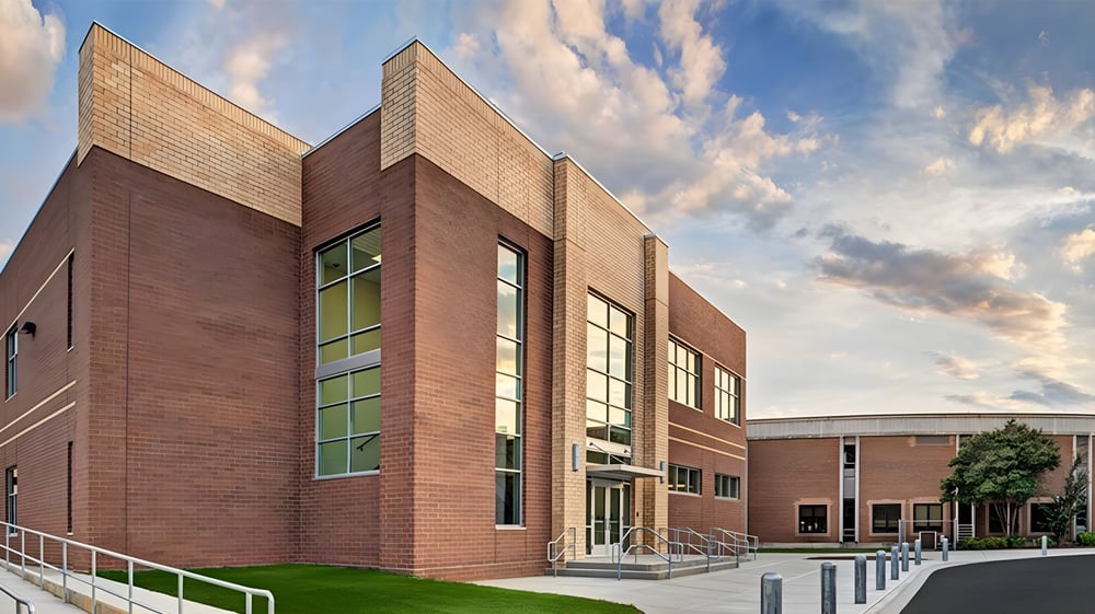 Das moderne Backsteingebäude der Charlotte-Mecklenburg Schools mit großen Fenstern und einer Rasenfläche im Vordergrund unter bedecktem Himmel.