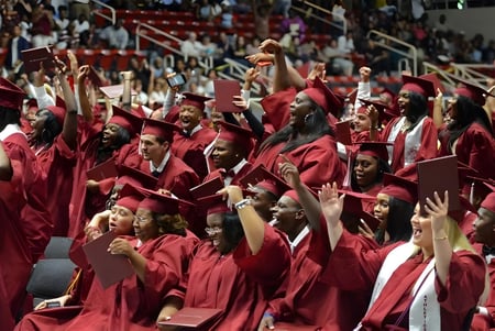 Absolventinnen und Absolventen der Charlotte-Mecklenburg Schools feiern ihre Abschlussfeier in roten Roben vor Bühne und Publikum.
