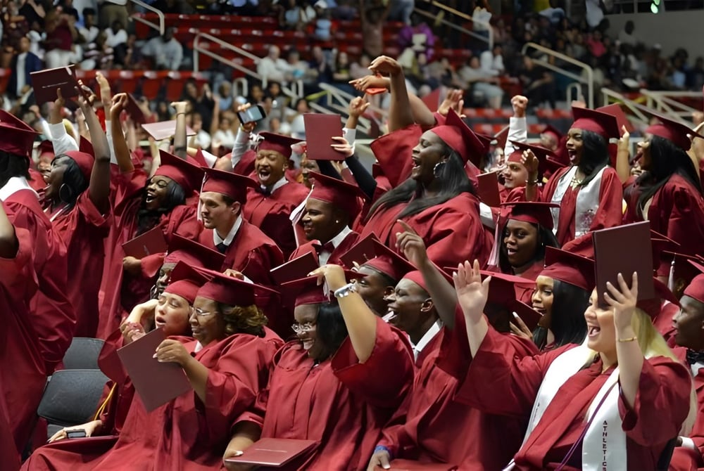 Absolventinnen und Absolventen der Charlotte-Mecklenburg Schools feiern ihre Abschlussfeier in roten Roben vor Bühne und Publikum.