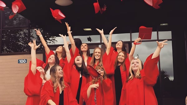 Schülerinnen der Charlottetown Rural High School heben in ihren roten Roben die Arme bei einem Bühnenauftritt.