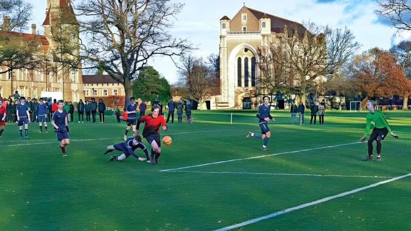 Eine Gruppe Schüler spielt Rugby auf dem Spielfeld der Charterhouse School vor einem historischen Gebäude.