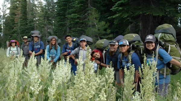 Eine Gruppe von Schülern der Charterhouse School steht mit Wanderkleidung auf einer Wiese mit hohem Gras und Wildblumen vor einem dichten Wald.