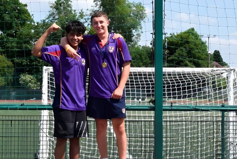 Zwei Schüler der Chase Grammar School stehen vor einem Fußballtor auf einem Rasenfeld mit Bäumen im Hintergrund.